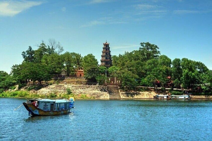 A traditional pagoda by a river with boats and lush greenery. 2