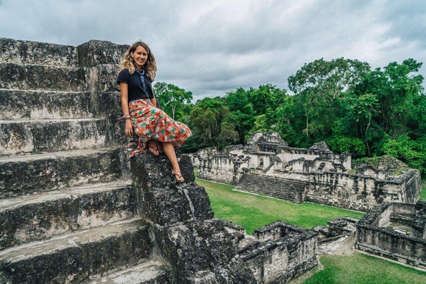 A person sitting on ancient stone steps surrounded by lush greenery and ruins. 1