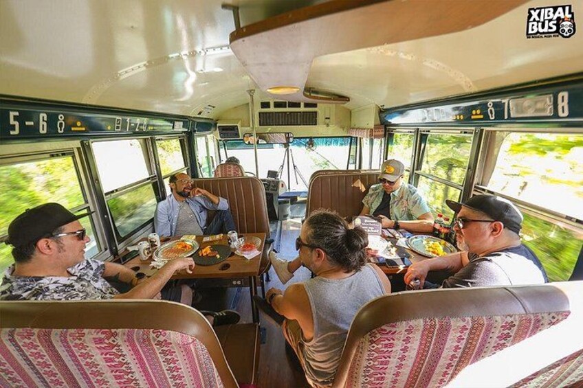 A group of people dining inside a bus with a view of greenery outside. 5