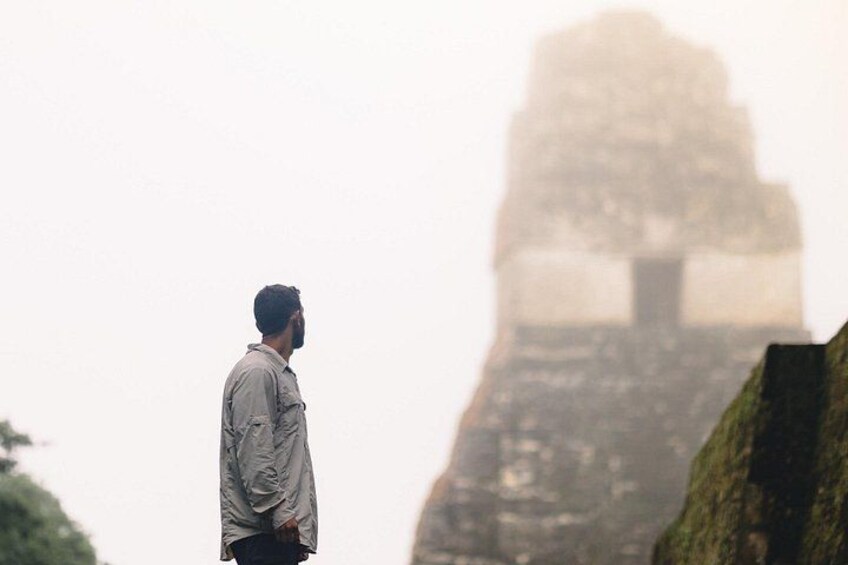 A person standing with a large, mist-covered structure in the background. 4