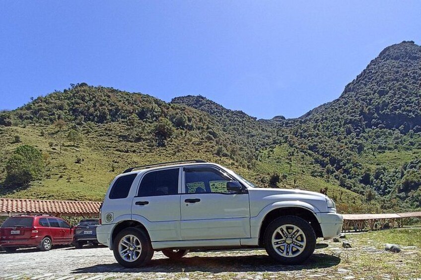 A white SUV parked on a gravel road with a mountainous backdrop. 2