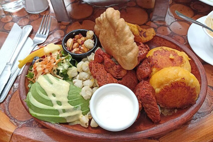 A plate of food with various items including a salad, sliced avocado, a bowl of nuts, and some fried items. 5