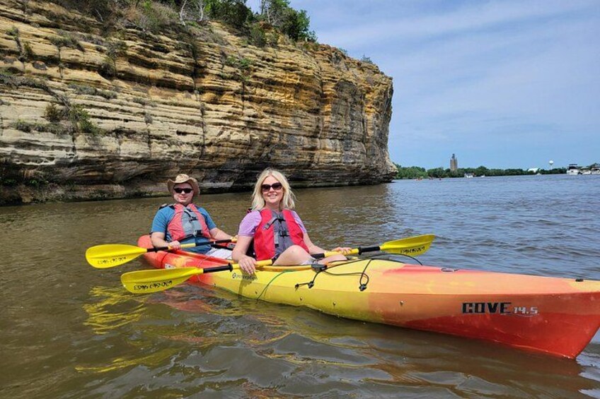 Two people kayaking on a calm river with rocky cliffs in the background. 4