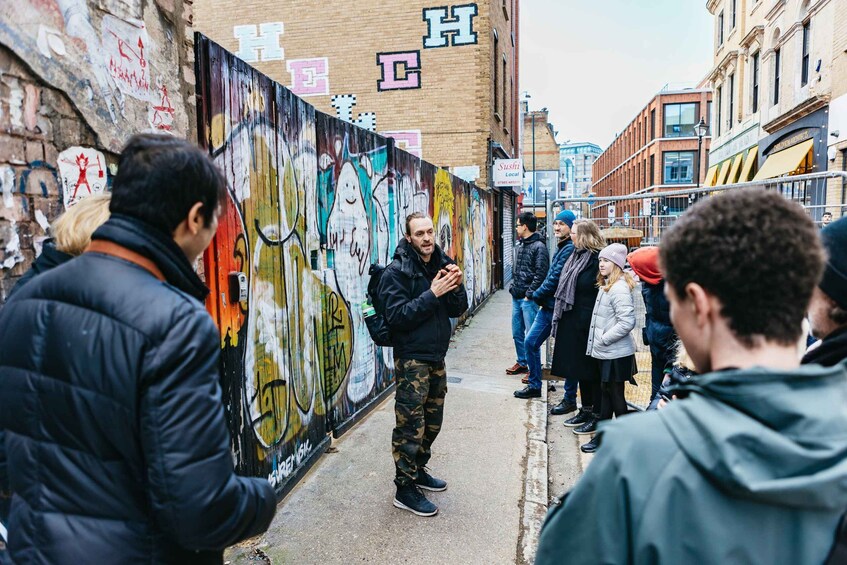 A group of people standing on a street with colorful graffiti on the walls. 2