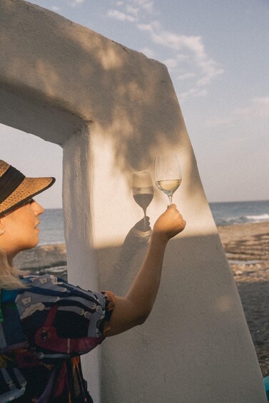 A person holding a wine glass, standing near a white structure by the beach. 4