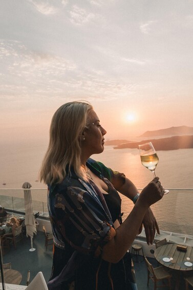 A person holding a glass of wine on a balcony overlooking a body of water during sunset. 3