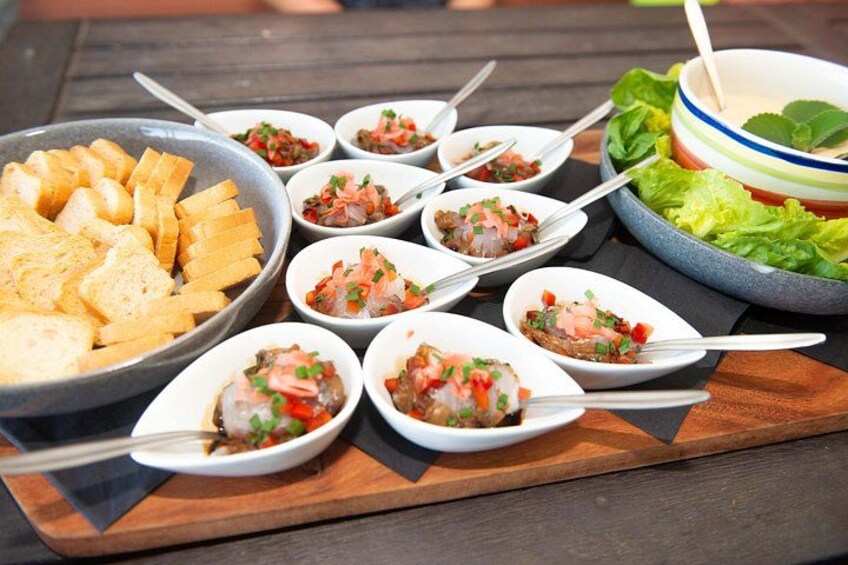 Een houten tafel met diverse gerechten, waaronder een kom met sneetjes brood, verschillende kleine kommetjes ceviche en een kom sla. 2