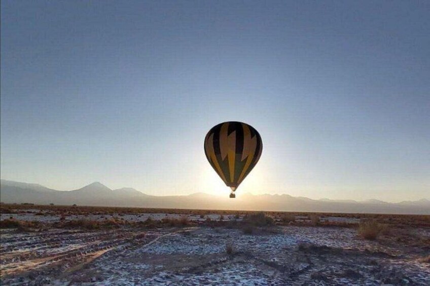 A hot air balloon over a barren landscape with mountains in the background. 1