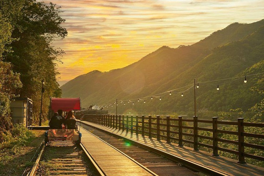 A train on tracks with a red canopy, surrounded by greenery and hills during sunset. 3
