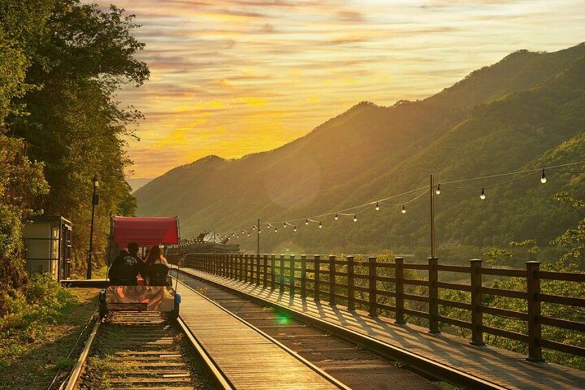 Een trein op rails, met een rood dak, omringd door groen en heuvels tijdens de zonsondergang. 4