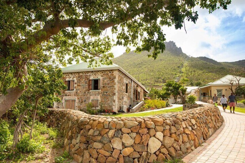 A stone building with a stone wall, a paved path, and a mountainous landscape in the background. 4
