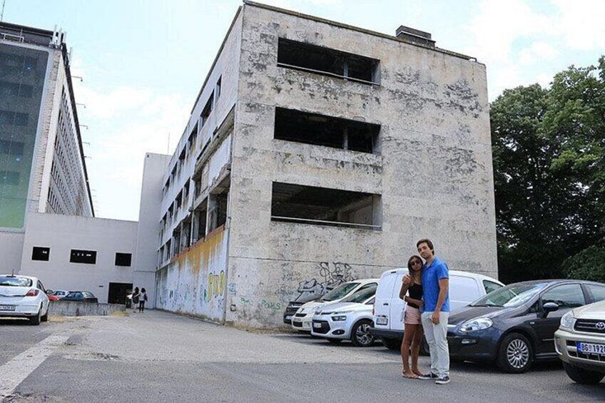 Un hombre y una mujer están de pie frente a un edificio con grafitis y coches aparcados. 3