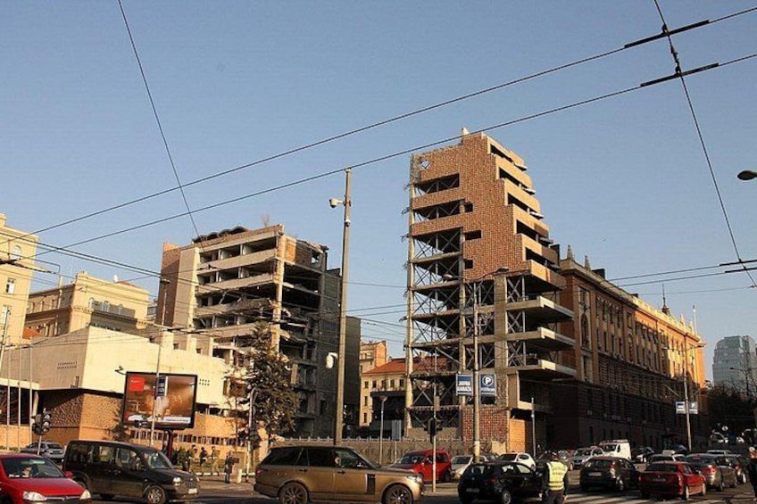 A busy urban street with cars, a multi-story building under construction, and other buildings in the background. 1