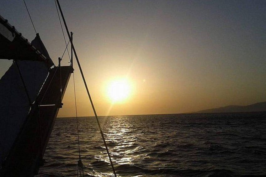 A boat with a sail, the sun setting over the ocean. 5