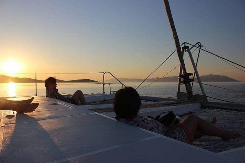 A sunset over a calm sea with a boat and people relaxing on the deck. 1