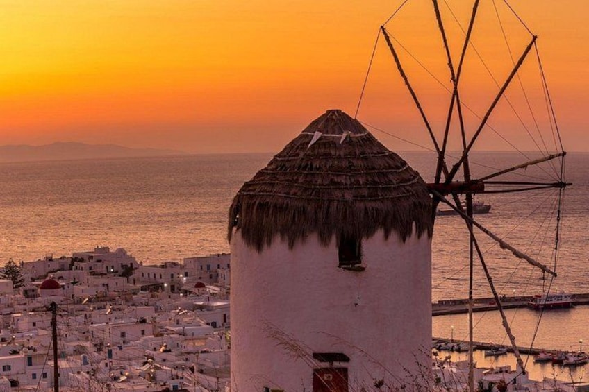A coastal village with white buildings, a traditional windmill, and a sunset over the sea. 3