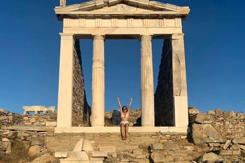 A person sitting in front of an ancient Greek temple with columns. 4