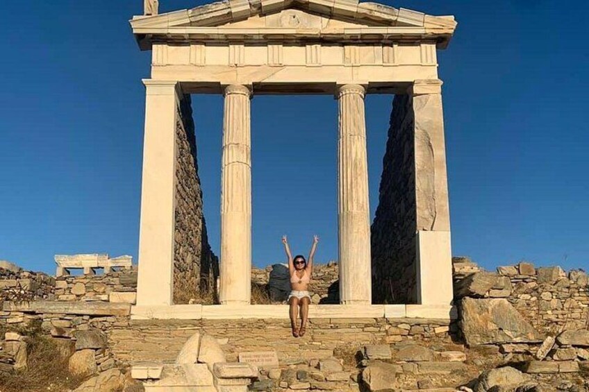 A person sitting in front of an ancient Greek temple with columns, surrounded by ruins. 5