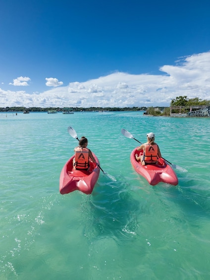 Two people kayaking on turquoise water with a clear sky and distant shoreline. 2