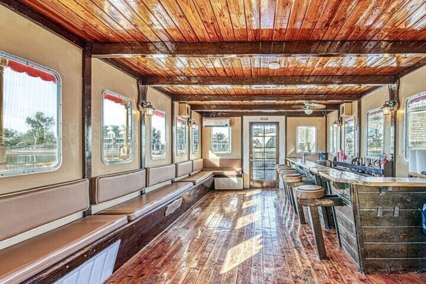 A train interior with wooden ceilings, bench seating, and a bar area. 2