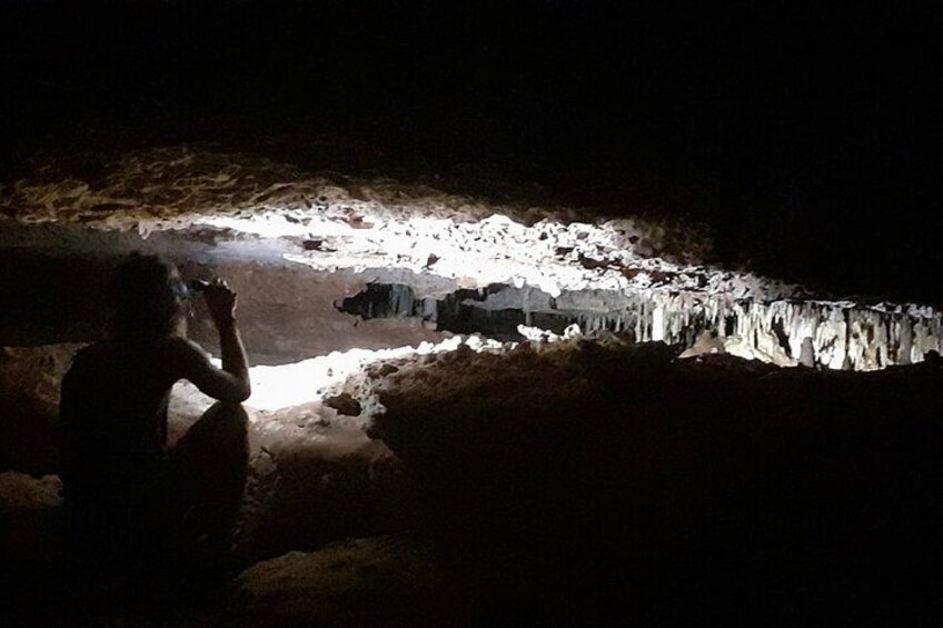 A person sitting in a cave with a flashlight illuminating a cave formation. 4