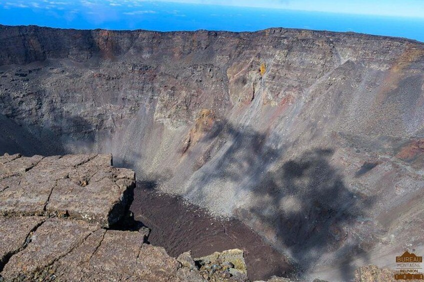 Un cratere vulcanico con un bordo roccioso e ripido, da cui si alza del fumo. 3