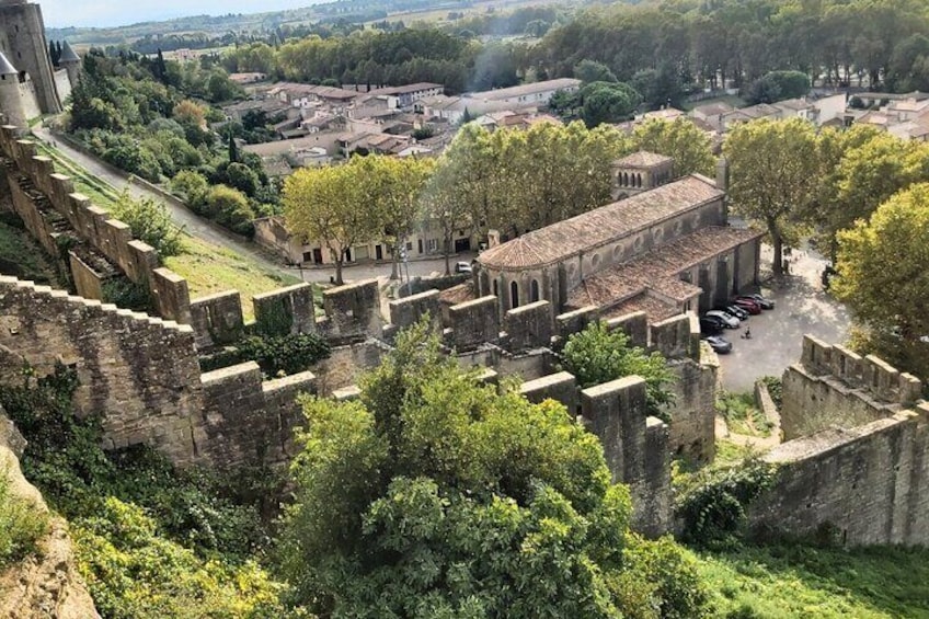 An ancient stone fortress with battlements, a central building with arches, and surrounding greenery. 1