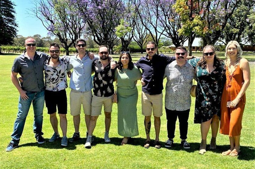 A group of people standing on grass with trees and a clear sky in the background. 4