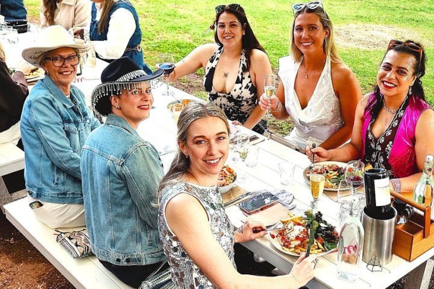 A group of people sitting at an outdoor table with food and drinks. 1