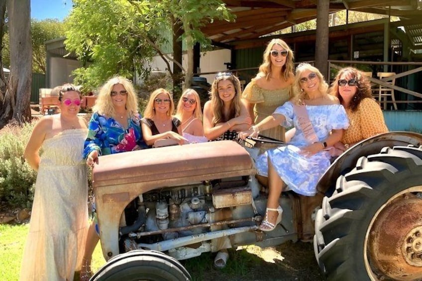 A group of people posing with a vintage tractor in a rural setting. 1