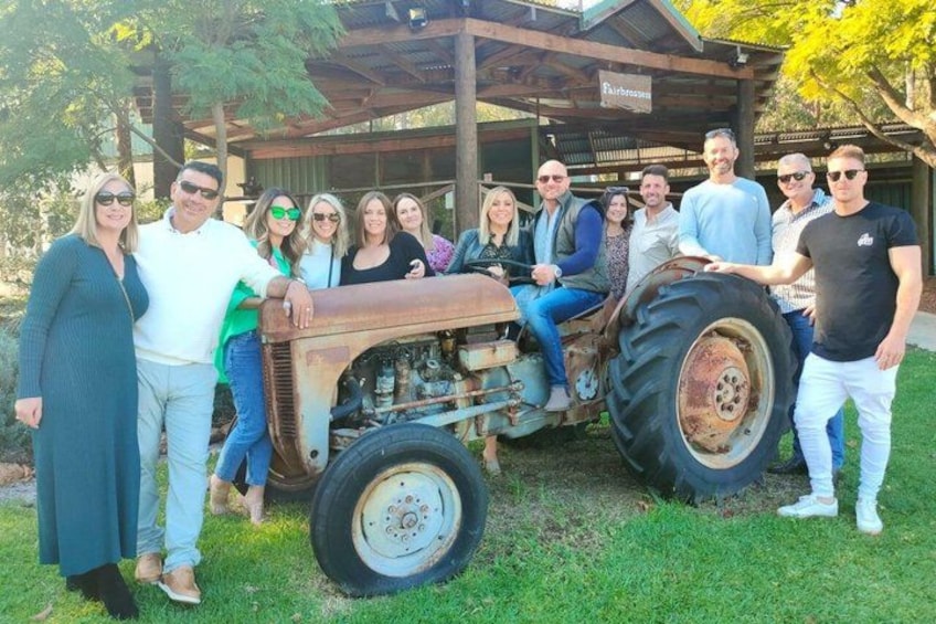 A group of people posing with a vintage tractor in a grassy outdoor setting. 2