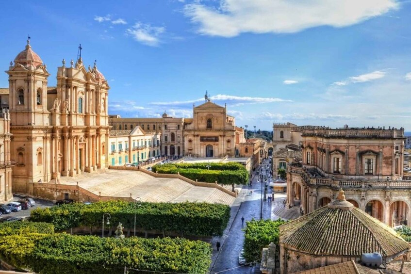 A historic plaza with ornate buildings, a central fountain, and a statue. 2