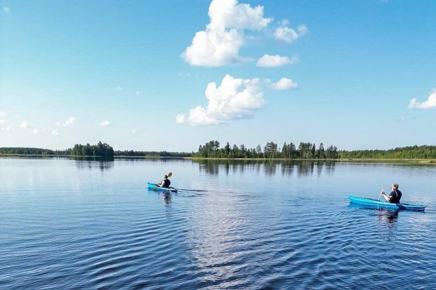 Dos personas haciendo kayak en un lago tranquilo, con cielo despejado y una línea de árboles en la distancia. 1