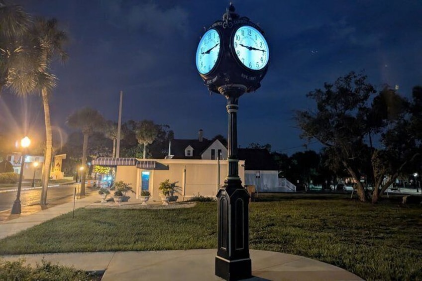 A clock tower with two faces, a building with a porch, and a well-lit street at night. 4