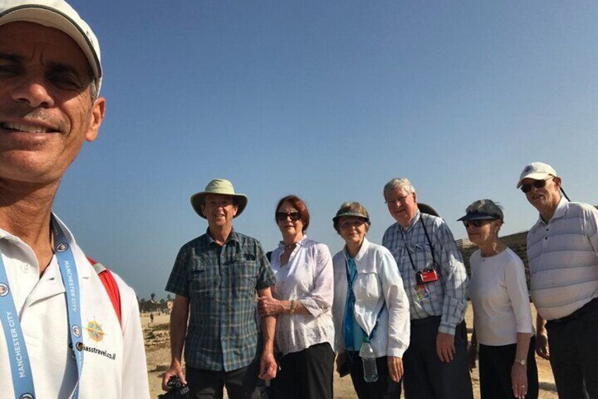 A group of people standing outdoors, some wearing hats and lanyards, with a clear sky in the background. 5