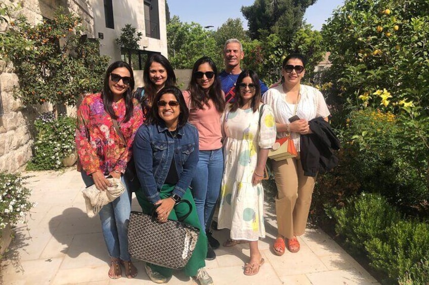 A group of people standing outdoors in a garden with stone walls and greenery. 1