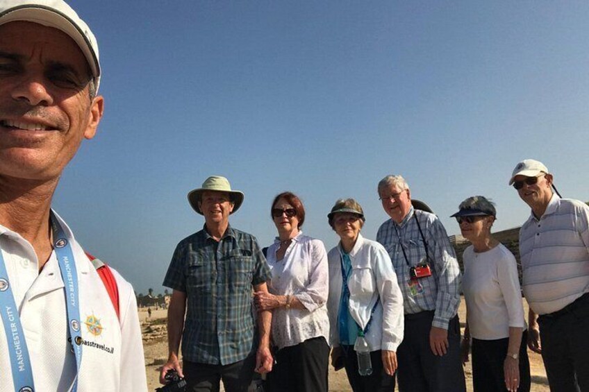 A group of people standing outdoors, some wearing hats and lanyards, with a clear sky in the background. 5