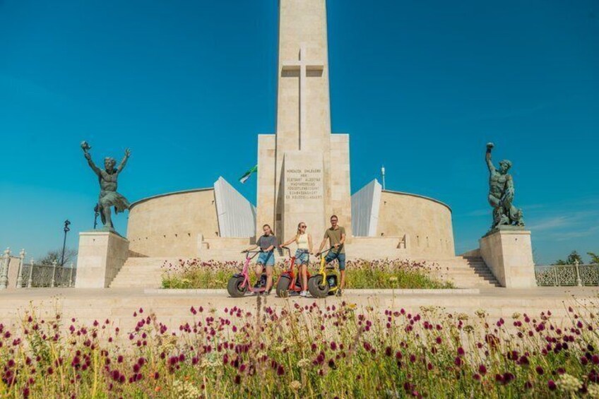 Un monumento con una cruz, rodeado de estatuas y personas sentadas en un banco. 2