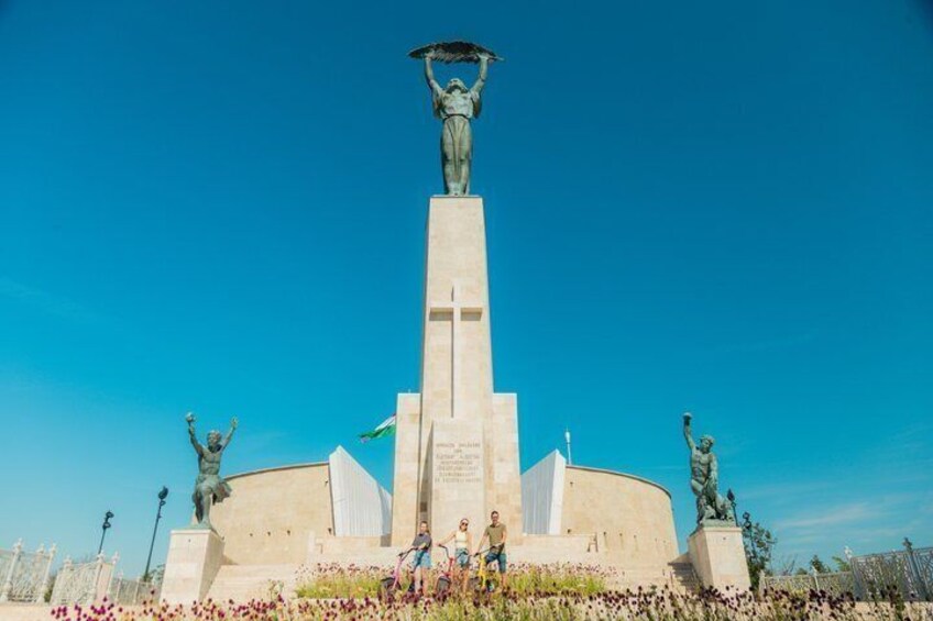 Un monumento con una estatua central, flanqueado por dos estatuas más pequeñas y un edificio circular con inscripciones. 1
