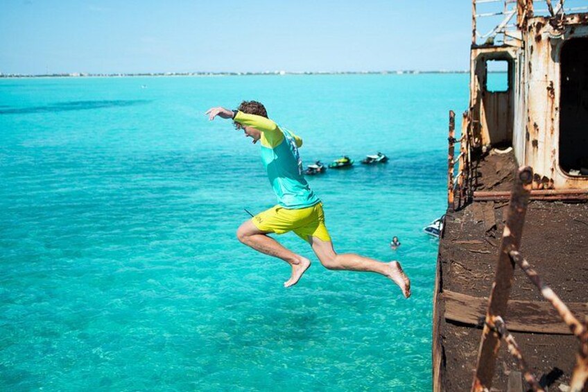 A person jumping off a rusty ship into turquoise water. 1