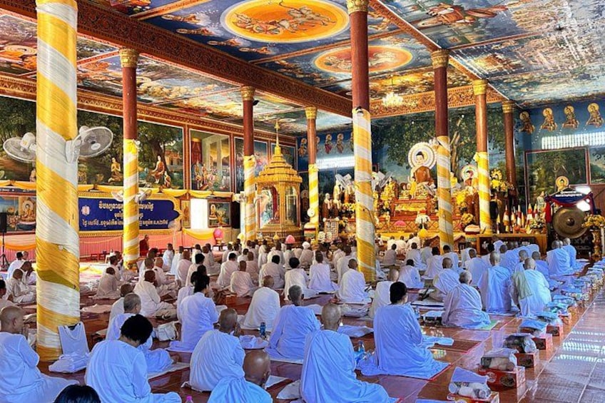Un grupo de personas vestidas de blanco sentadas en filas dentro de un templo con techo decorado y pilares dorados. 3