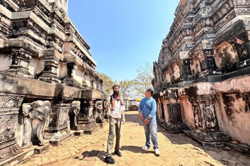 Two people standing in front of ancient stone structures with intricate carvings. 2