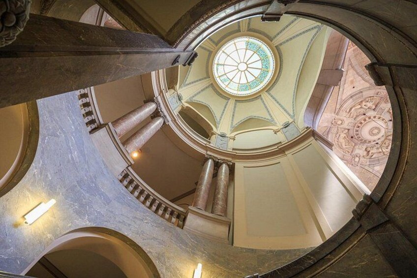 Een statig architectonisch interieur met een koepelplafond, een wenteltrap en rijke wanddecoraties. 3