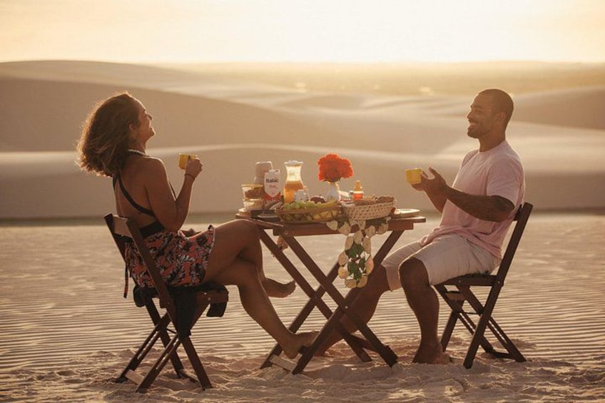 Two people sitting at a table with food and drinks in a desert setting. 4