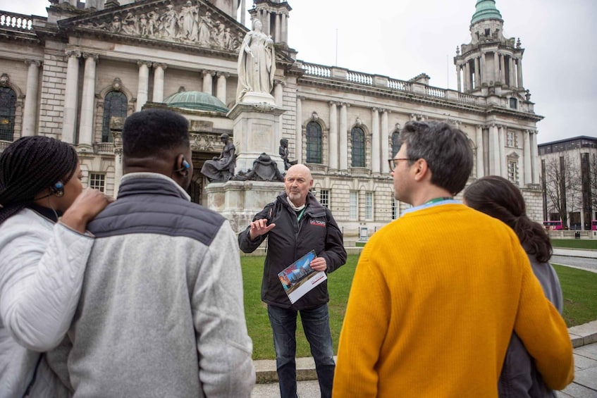 Un groupe de personnes se tient devant un bâtiment historique à l’architecture classique, orné de colonnes et de statues. 3