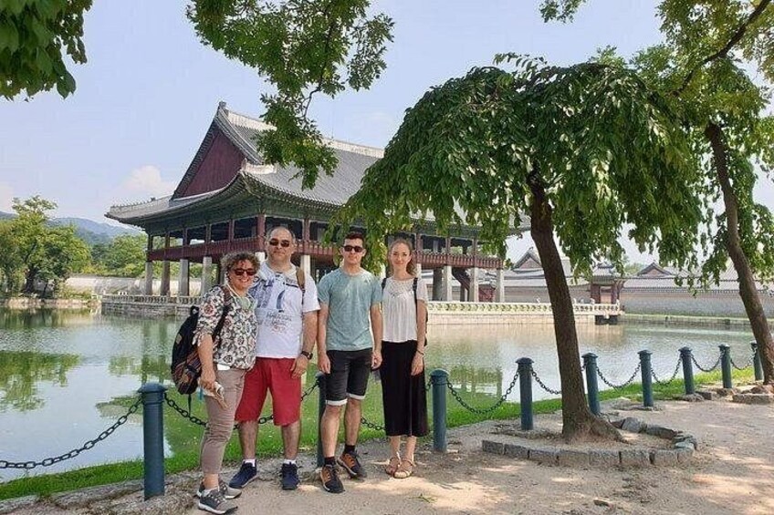 A group of people standing by a traditional building with a pond in the background. 1