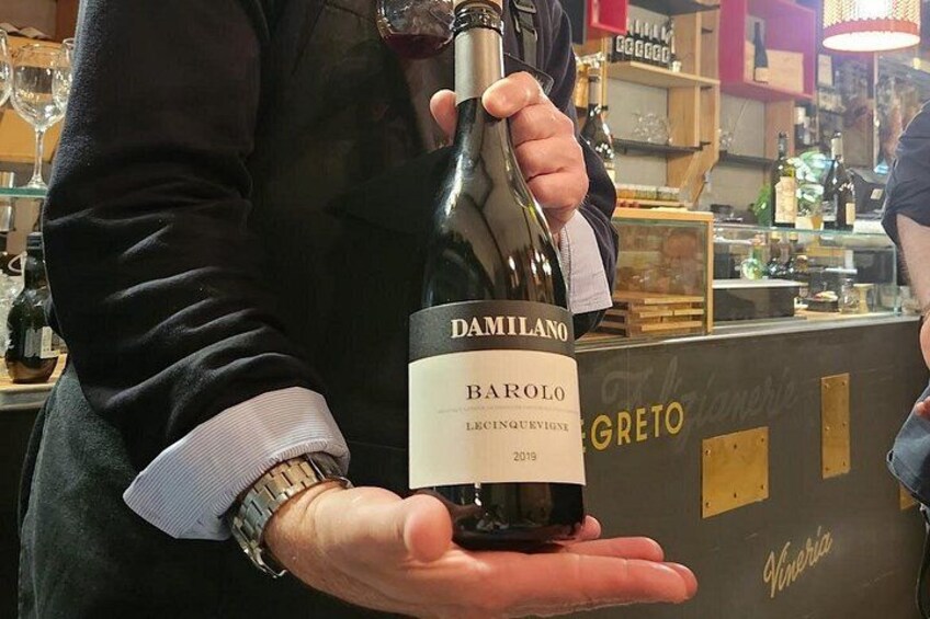 A person holding a bottle of wine with a label that reads 'DAMILANO BAROLO LECCEINQUERVIGNIE 2019 GRETO'. 2