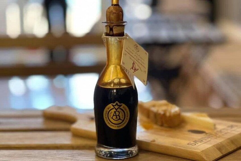A bottle of dark liquid with a gold cap and a tag, placed on a wooden surface with a piece of bread nearby. 2