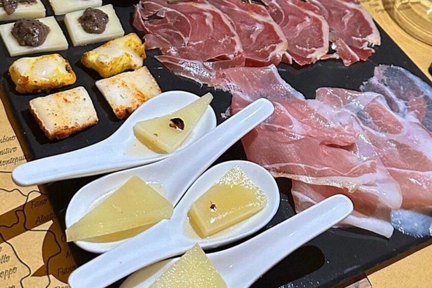 Ett urval av olika sorters lufttorkat kött och ostar, presenterat på ett svart fat. 5