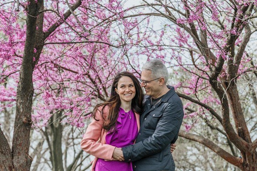 A couple embracing in front of blooming pink trees. 2